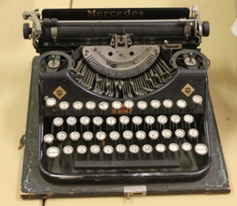 Vintage black Mercedes typewriter with round white keys on a beige surface.
