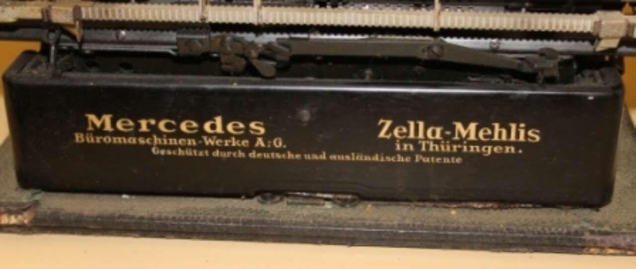 Black Mercedes-branded sign with gold text reading “Zella-Mehlis” on a metal machine or display case