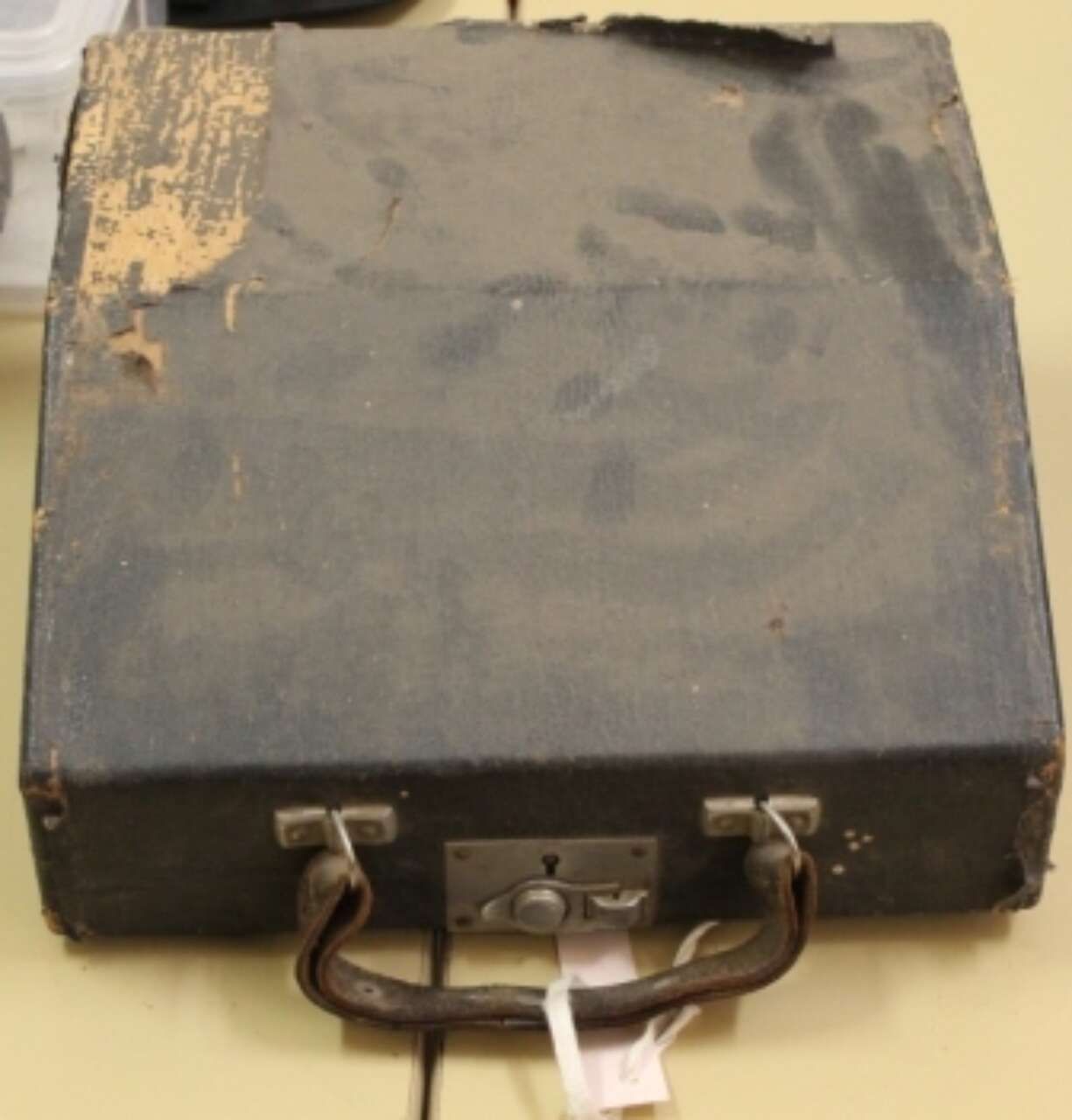 Worn black briefcase with scuffed edges and a metal latch, shown closed on a light background