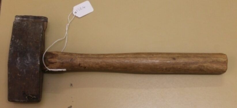 Brown-handled sledgehammer with a dark metal head on a beige surface, with a small tag attached.
