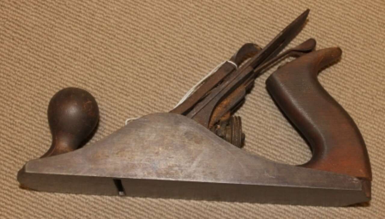 Vintage hand plane tool with wooden body and metal blade on a beige background