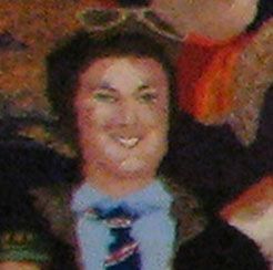 Person smiling in a dark suit and striped tie against a blurred crowd background