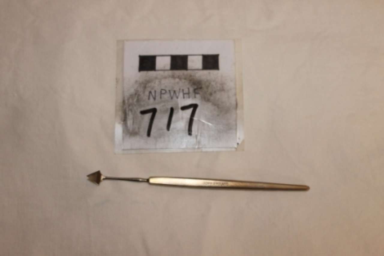 Small evidence placard labeled “Alpha 717” above a gold pen-like object on a beige surface