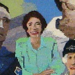 Smiling person in a light green jacket in a group photo, with other people partially visible around them.