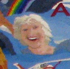 Smiling blond cartoon character in a blue shirt under a rainbow with red lettering