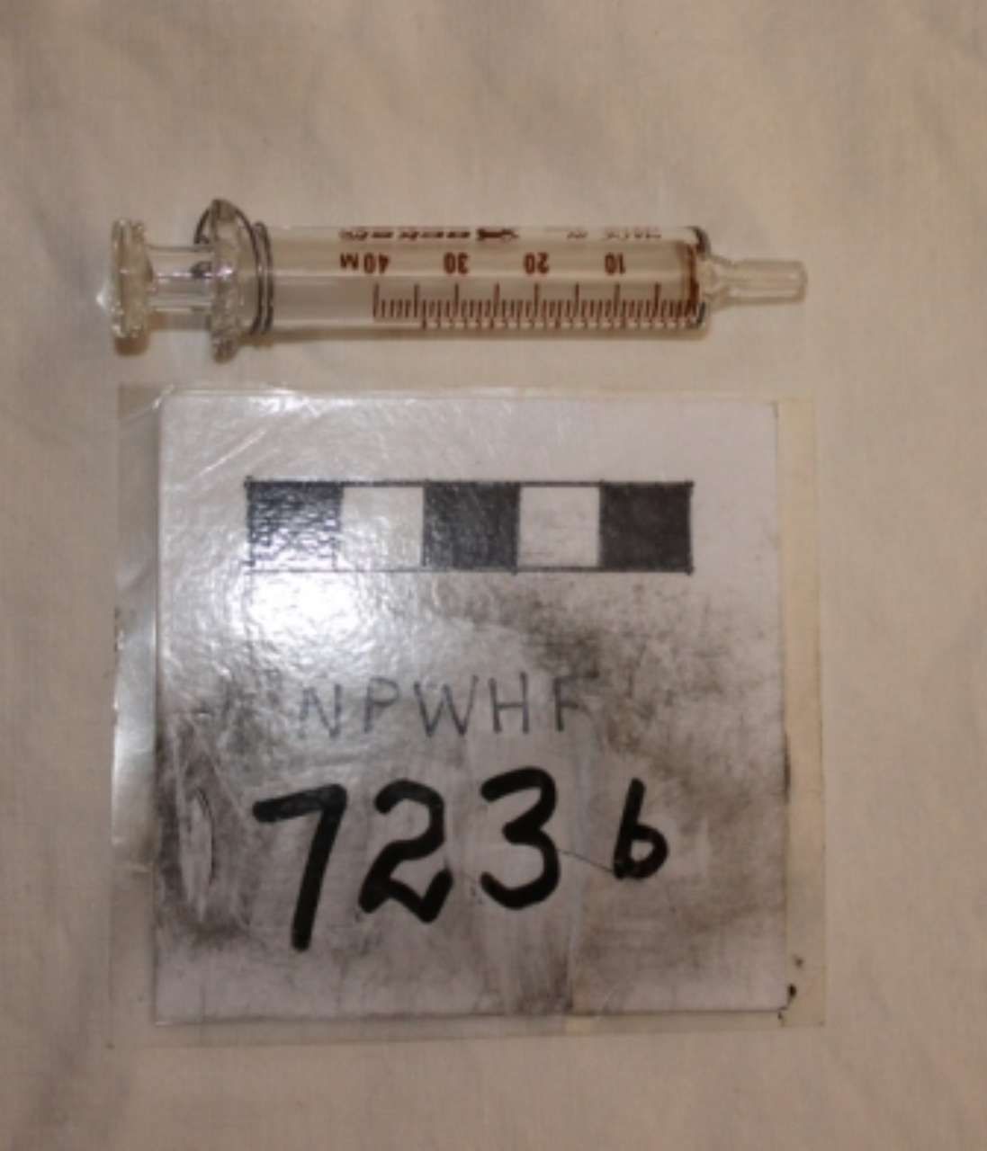 A syringe above a clear evidence bag labeled “7236” with a black-and-white scale.