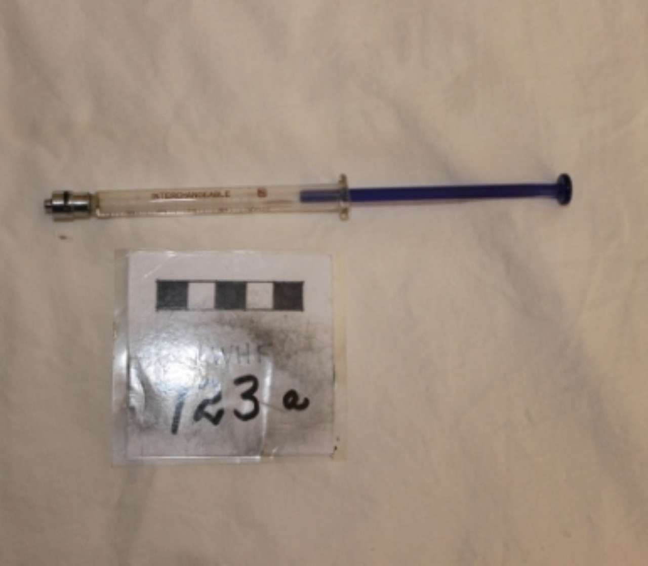 Syringe with a blue plunger lying above a small numbered label on a plain background