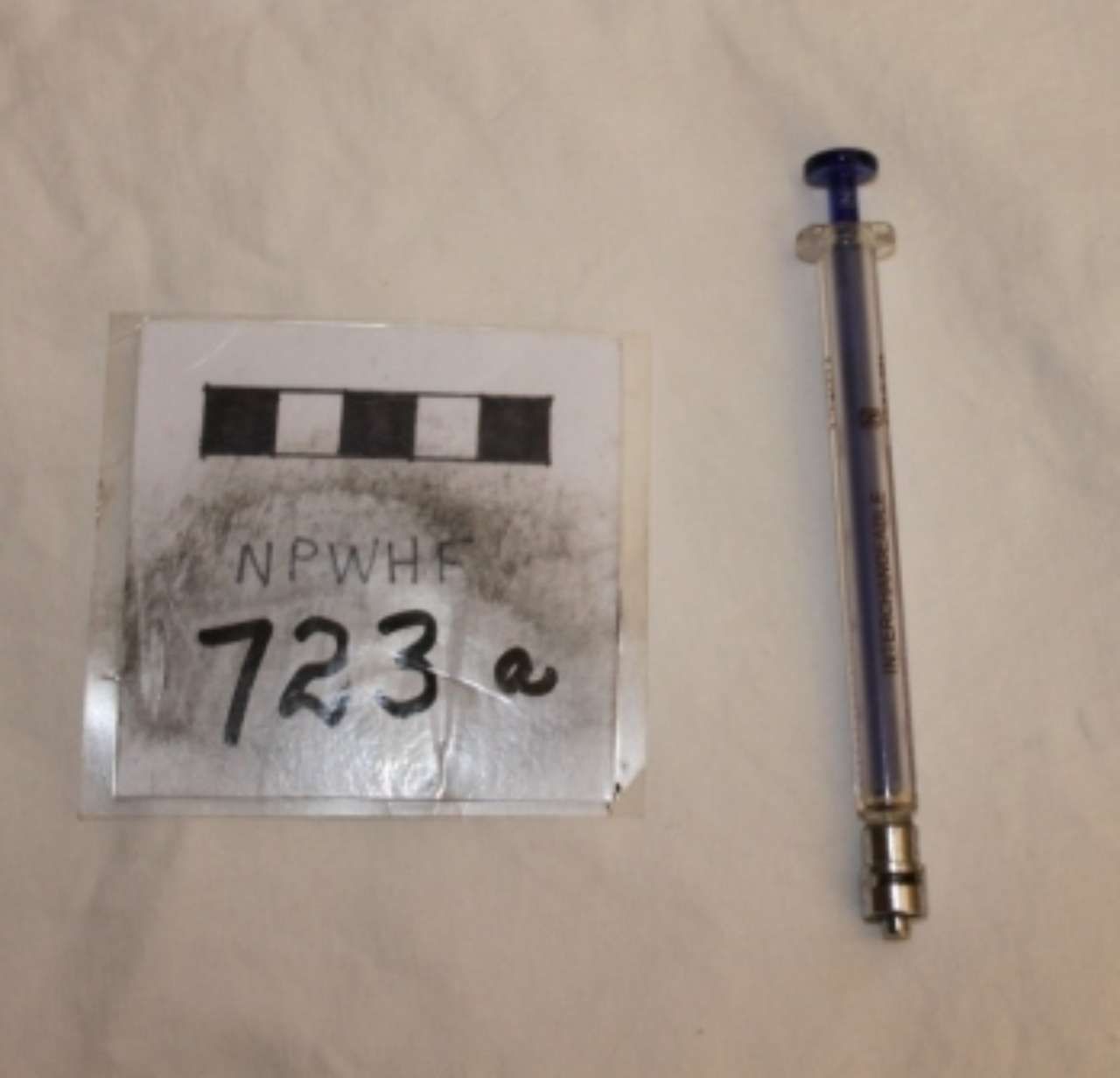 Transparent blue syringe beside a labeled evidence card marked “NPWH 723 e”