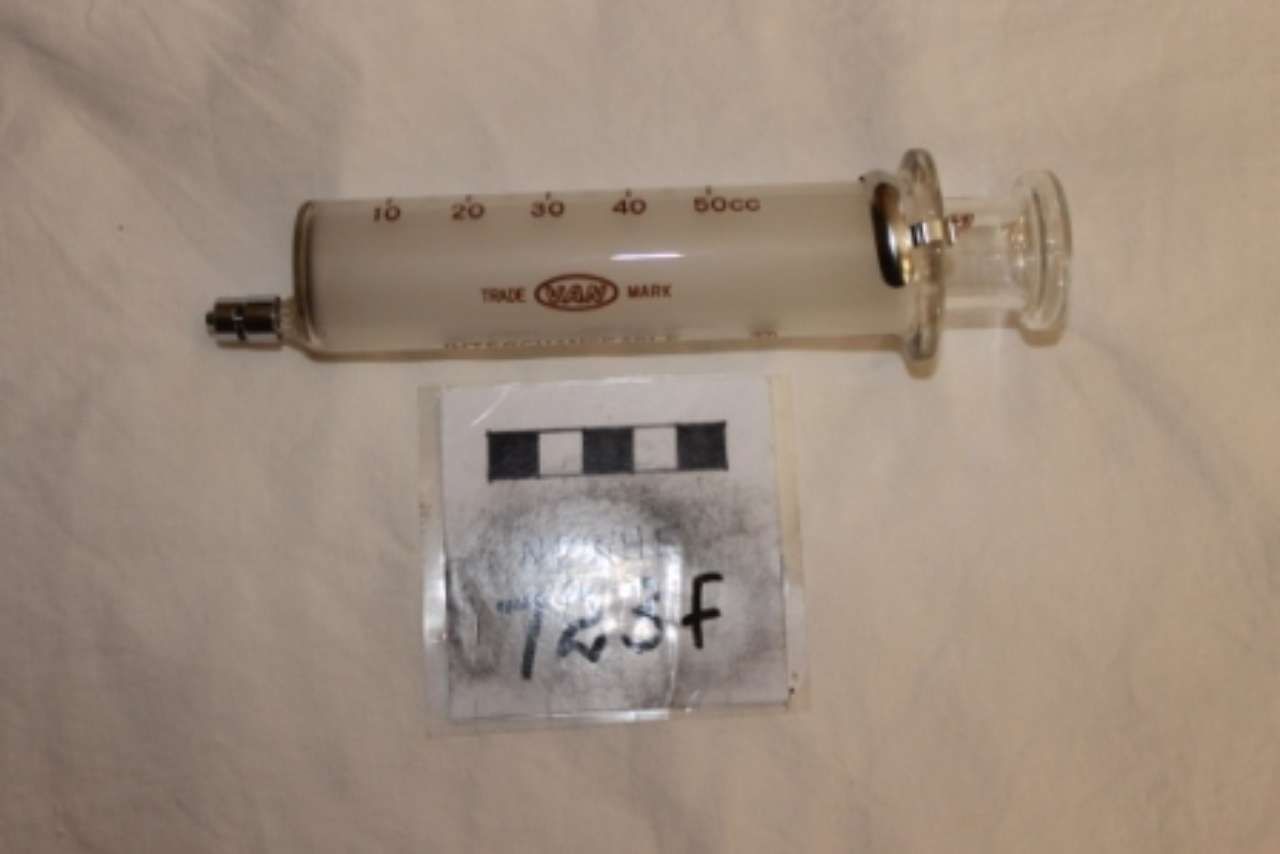 Small clear glass syringe-like vial with black plunger on a white background, labeled “Trof.”