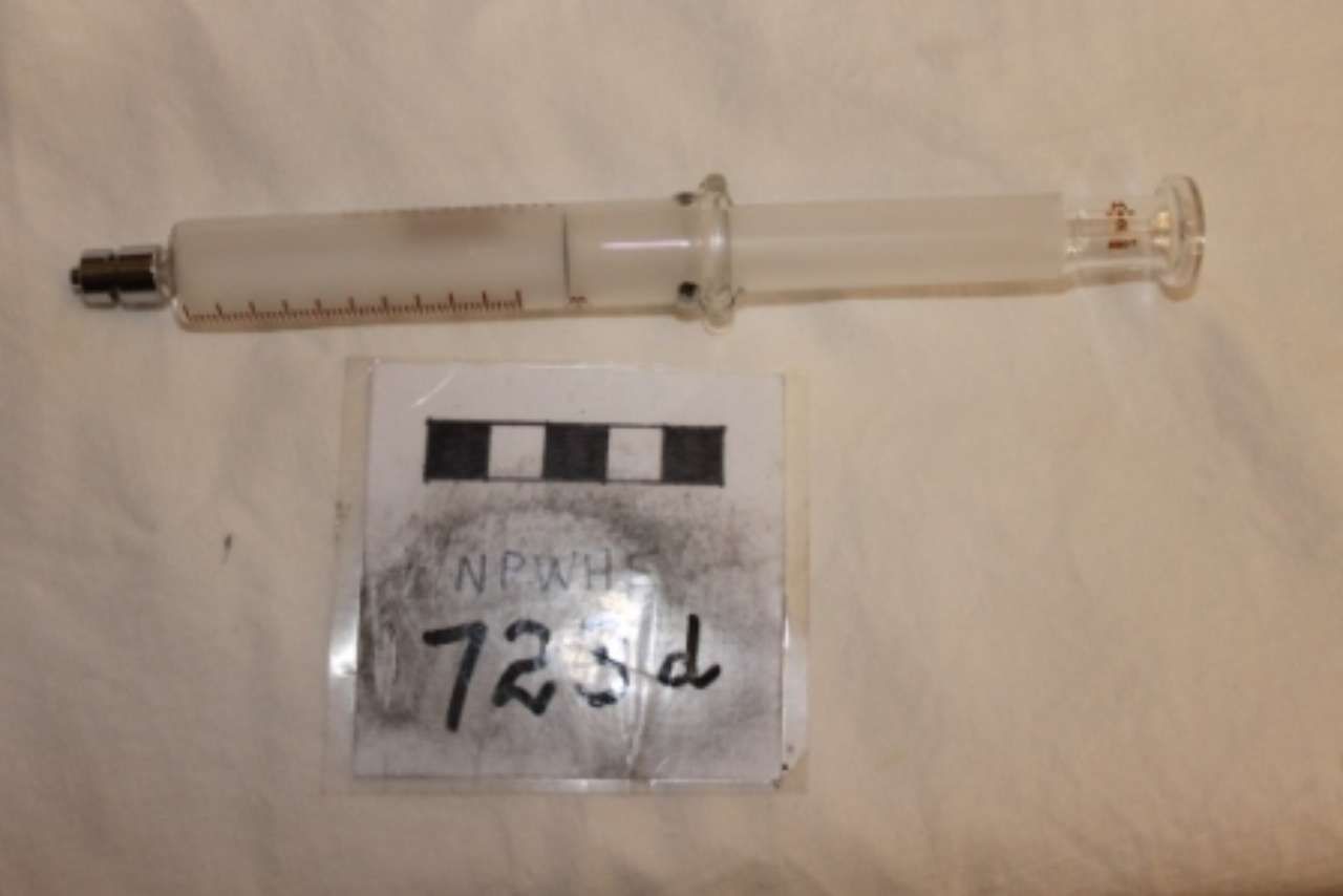 Used syringe beside a small handwritten label on a light surface
