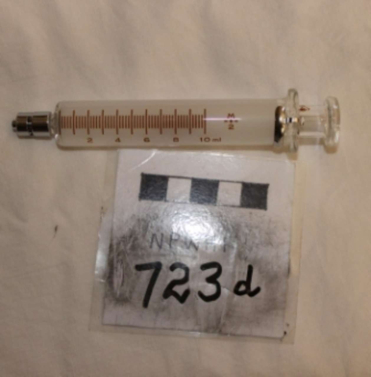Syringe with measurement markings beside a labeled evidence tag reading “723d”
