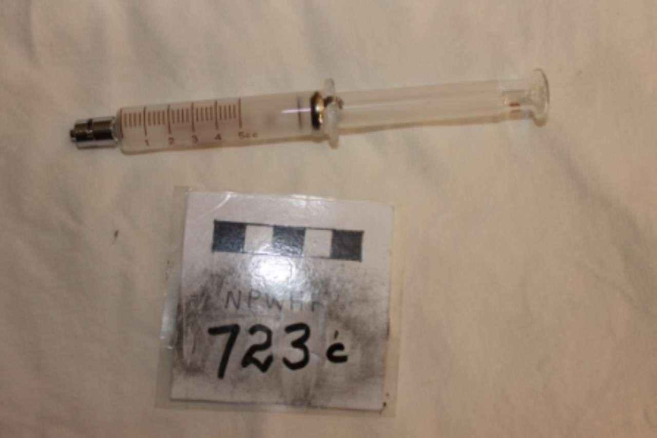 A clear syringe and a small labeled packet with “723c” on a white surface.