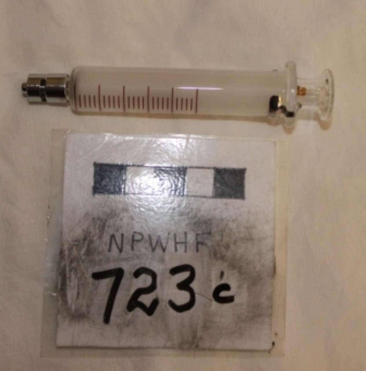 Small syringe with measurement markings above a labeled card reading “723c”