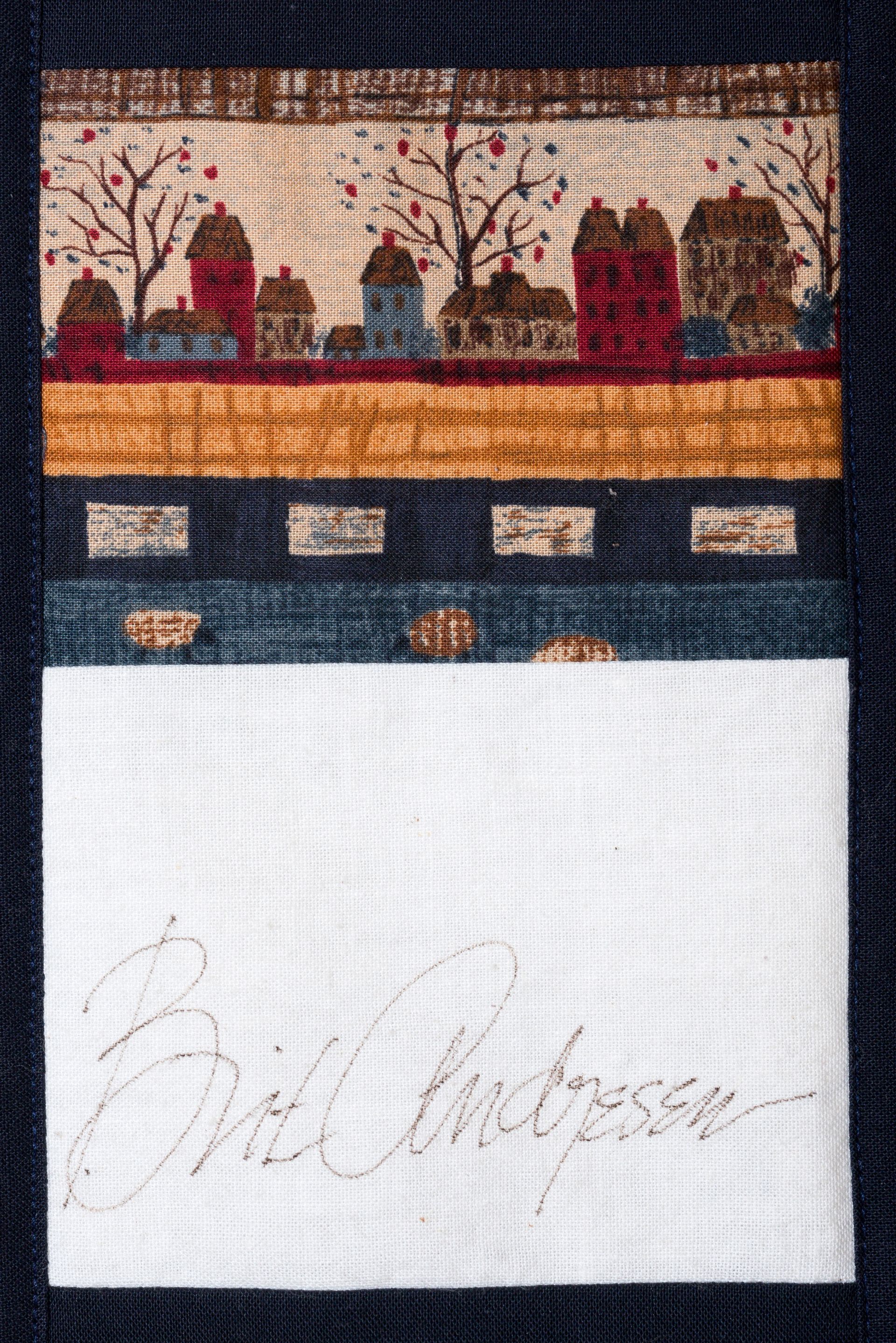 Embroidery sampler with colorful village scene above a white stitched signature panel
