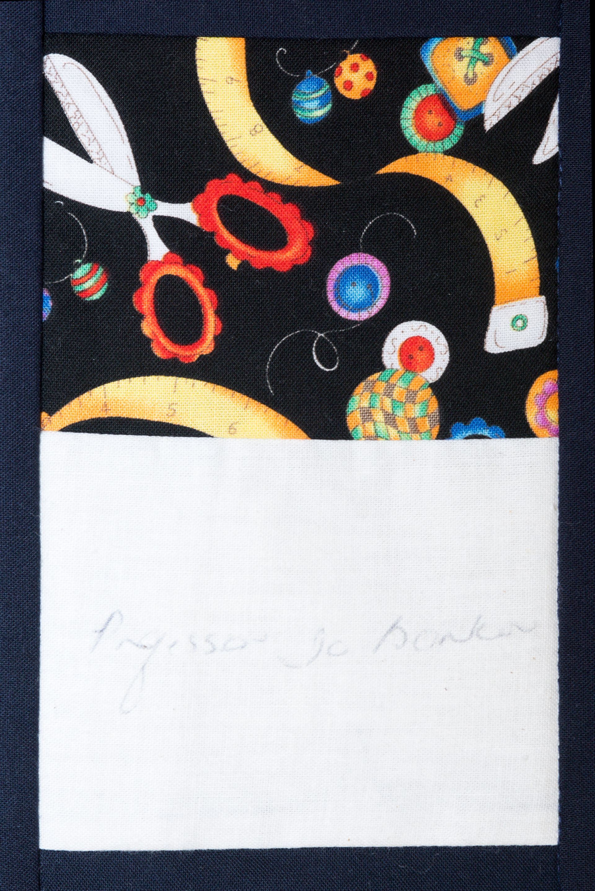 Dark patterned fabric with colorful rings and a white label panel below, faintly handwritten.