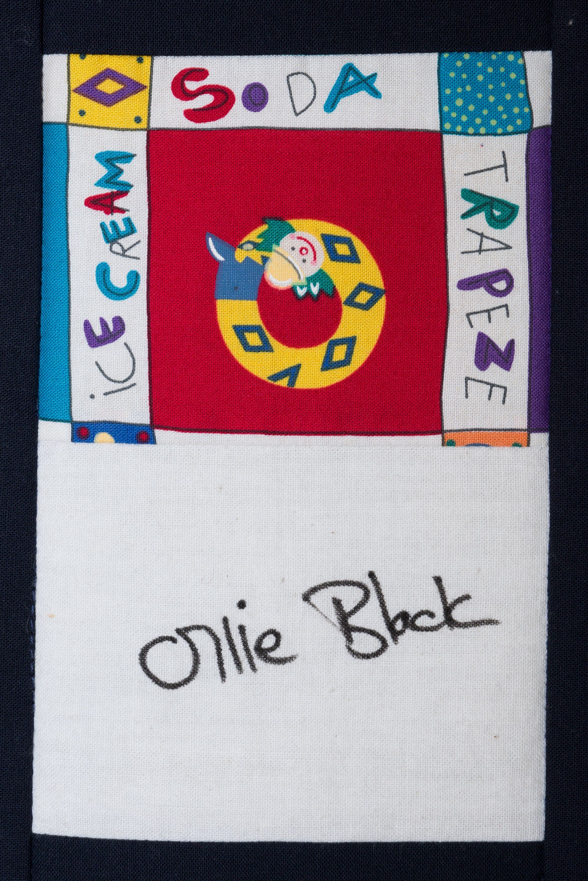 White fabric with a colorful flag patch and handwritten “Ollie Black” below.