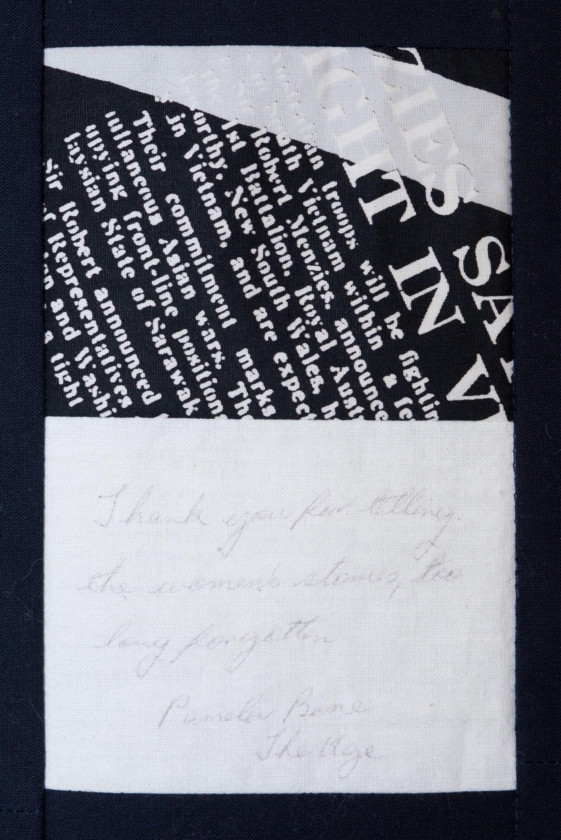Close-up of a black fabric label with white text partially covered by a blank white square.