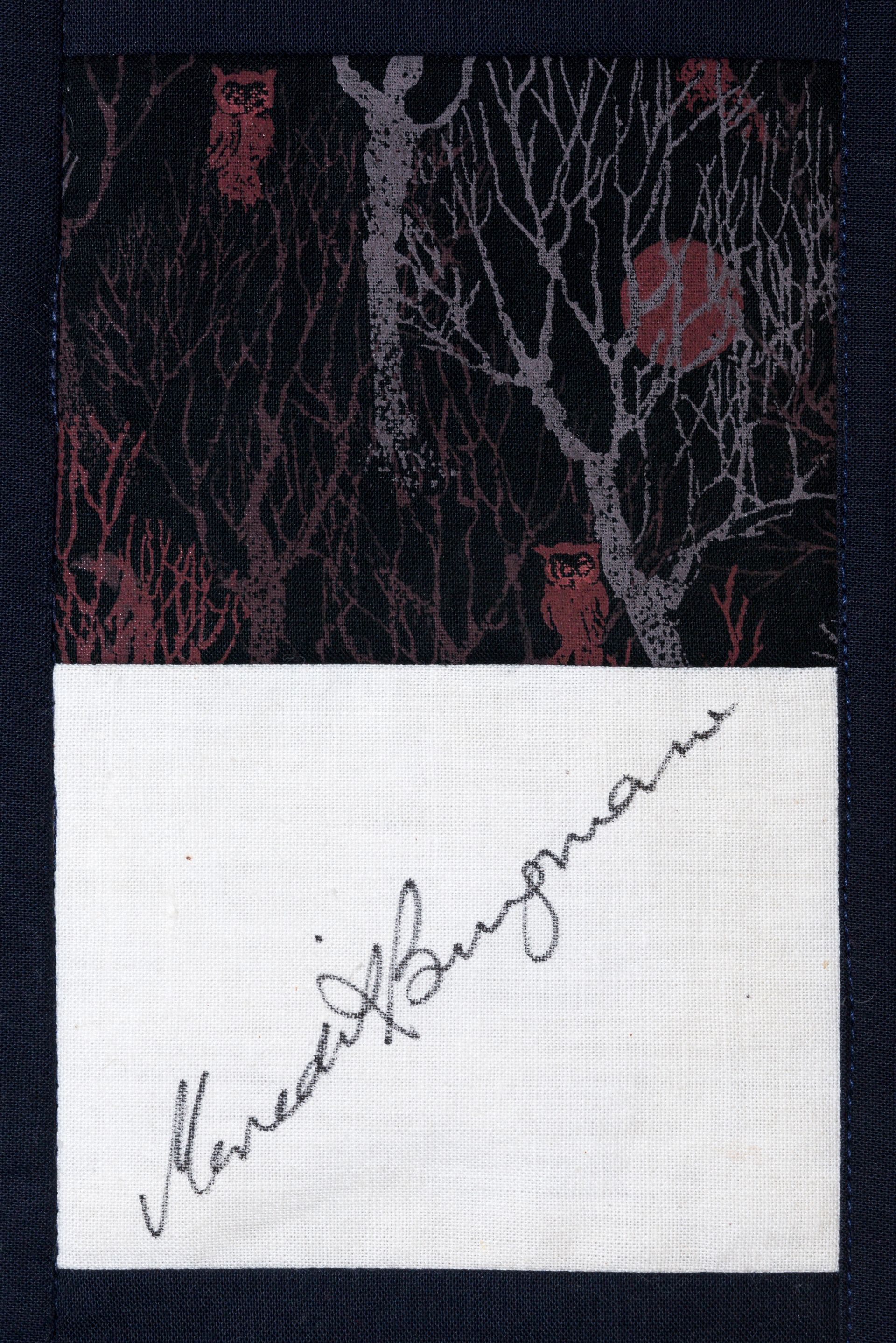 White note with handwritten signature on dark patterned fabric background