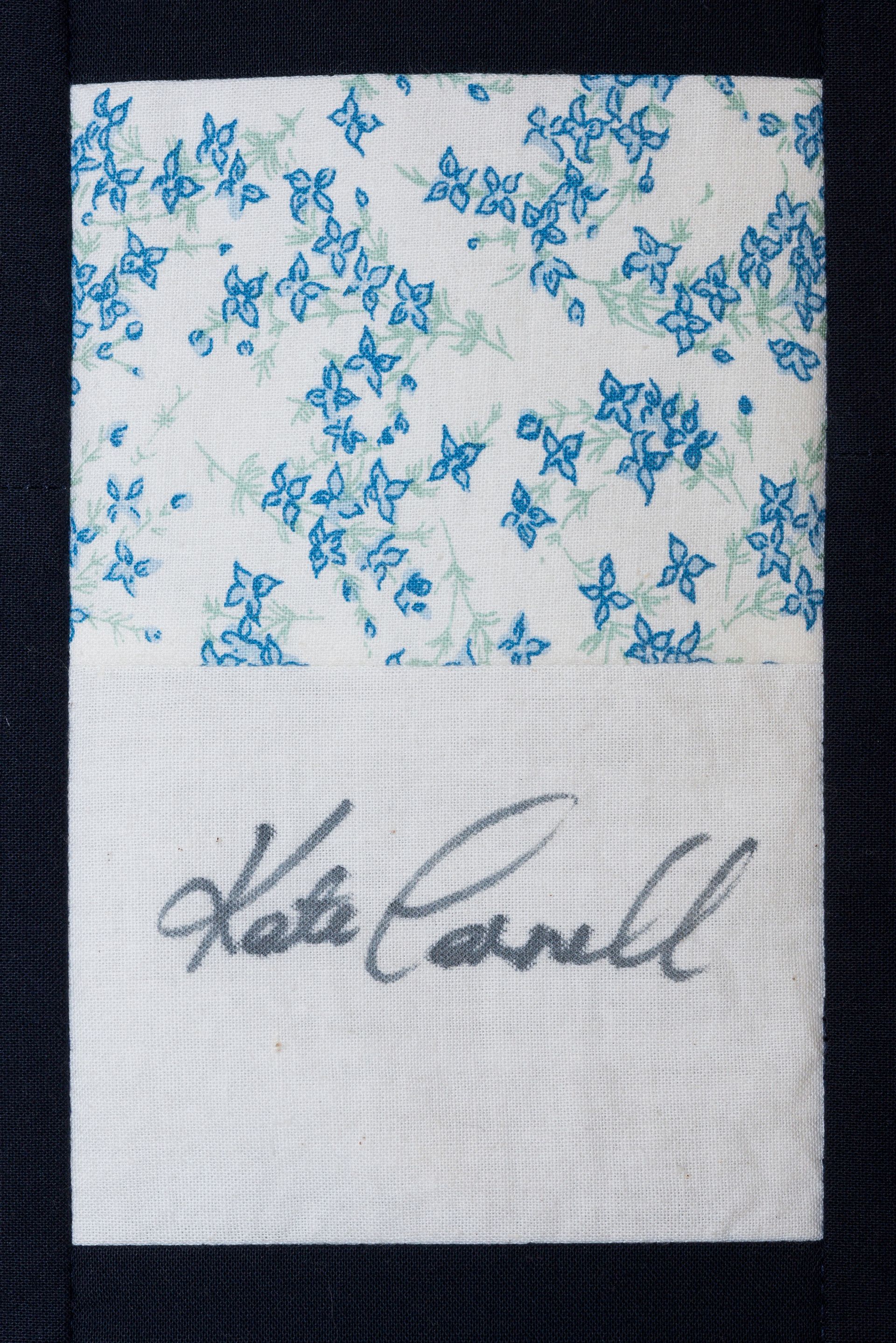 White fabric with blue floral print and a handwritten signature near the bottom.
