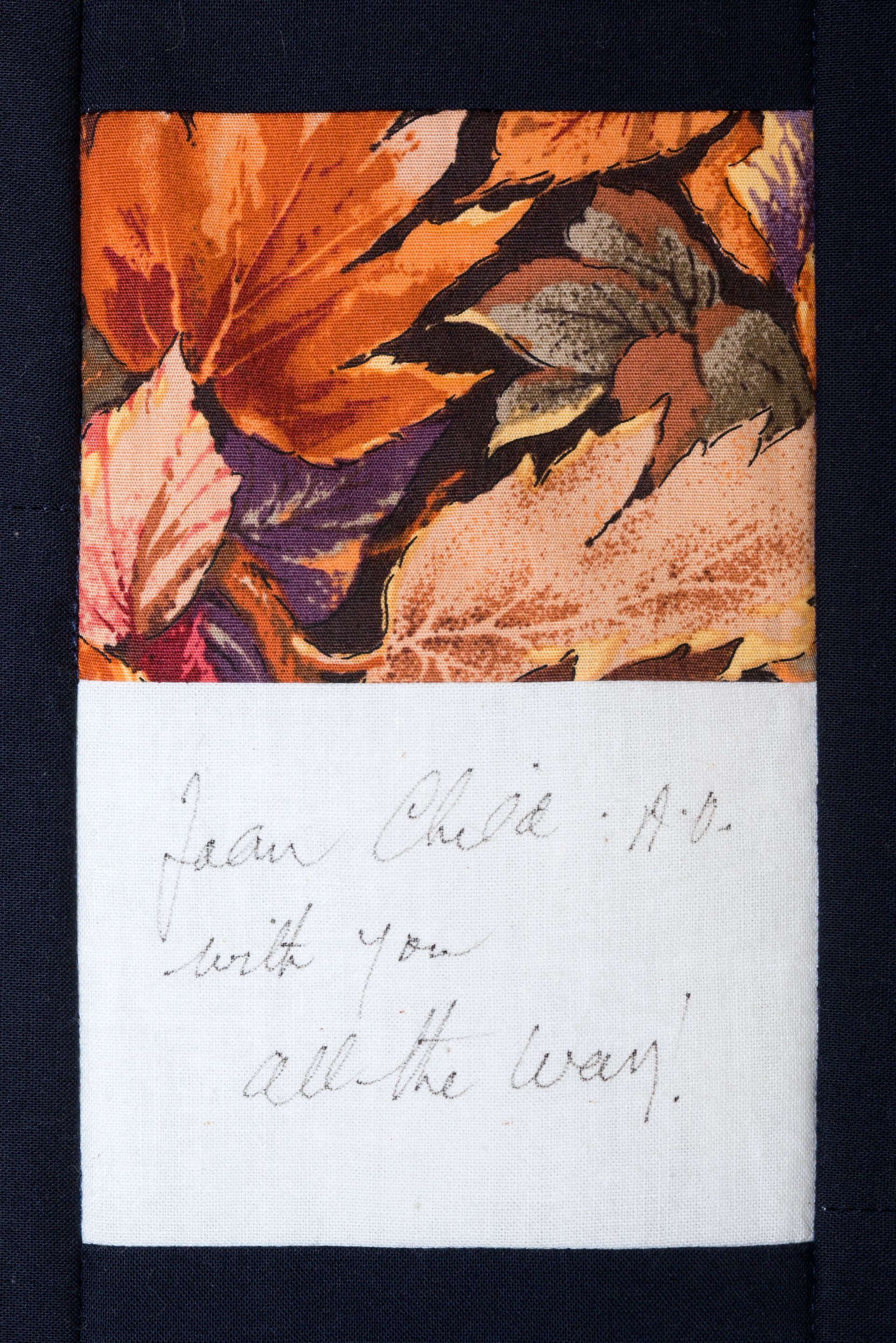 Close-up of a small fabric note with faded handwritten text beneath a colorful autumn leaf pattern.