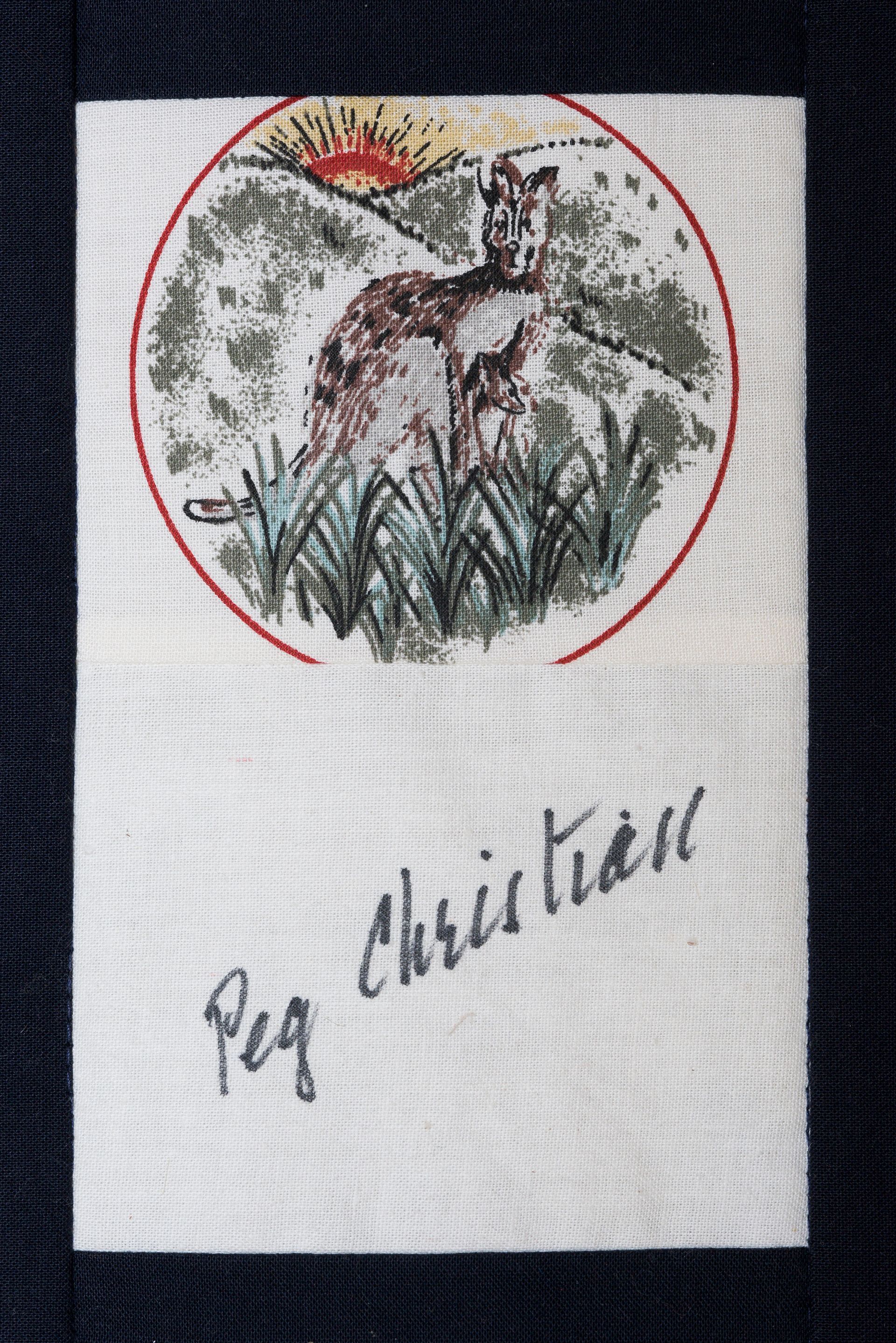 A small embroidered deer in a red oval with “Merry Christmas” stitched below.
