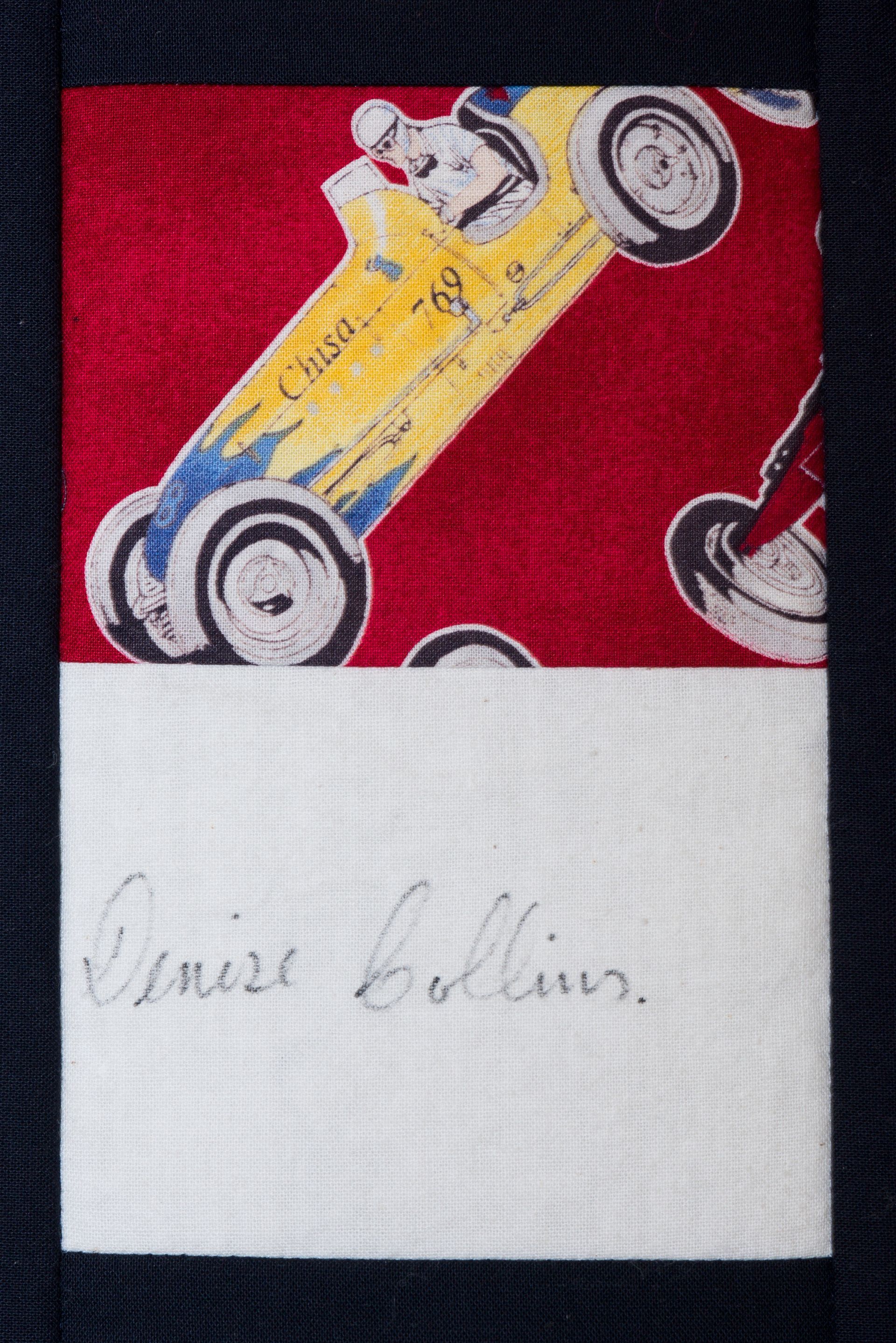 Red and white fabric patch with a yellow race car illustration and faint handwritten text.