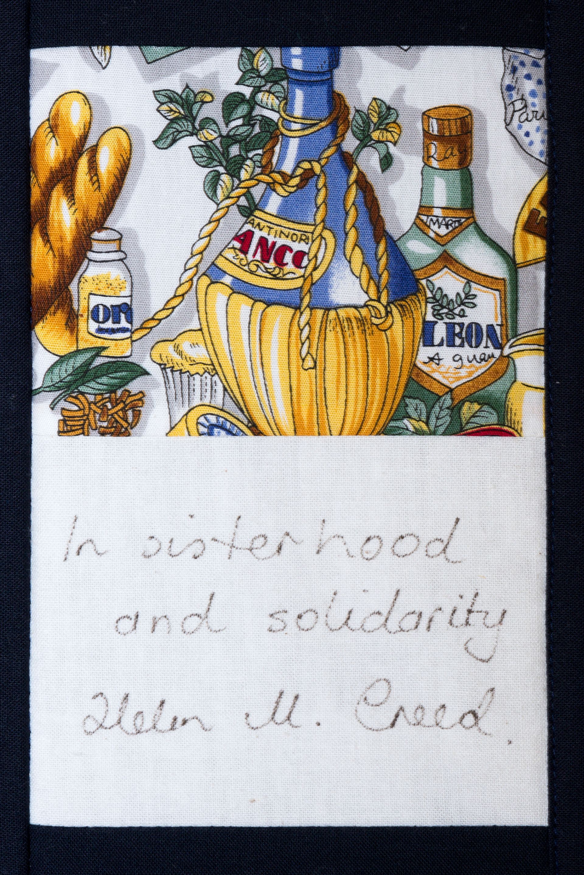 Embroidered wine and bread with handwritten note on white fabric, recalling the Last Supper.