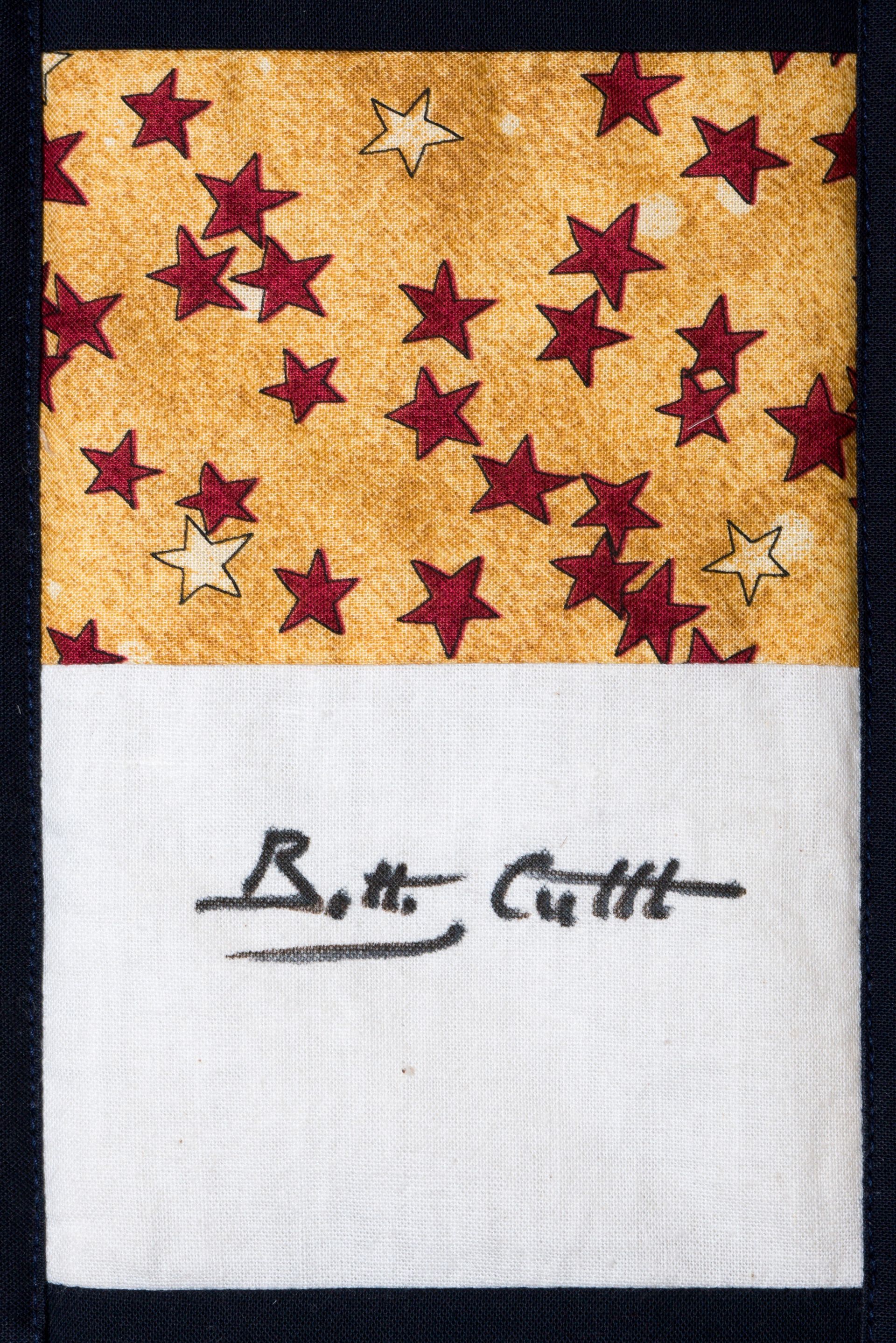 Gold fabric with red and white stars above a handwritten signature on white paper