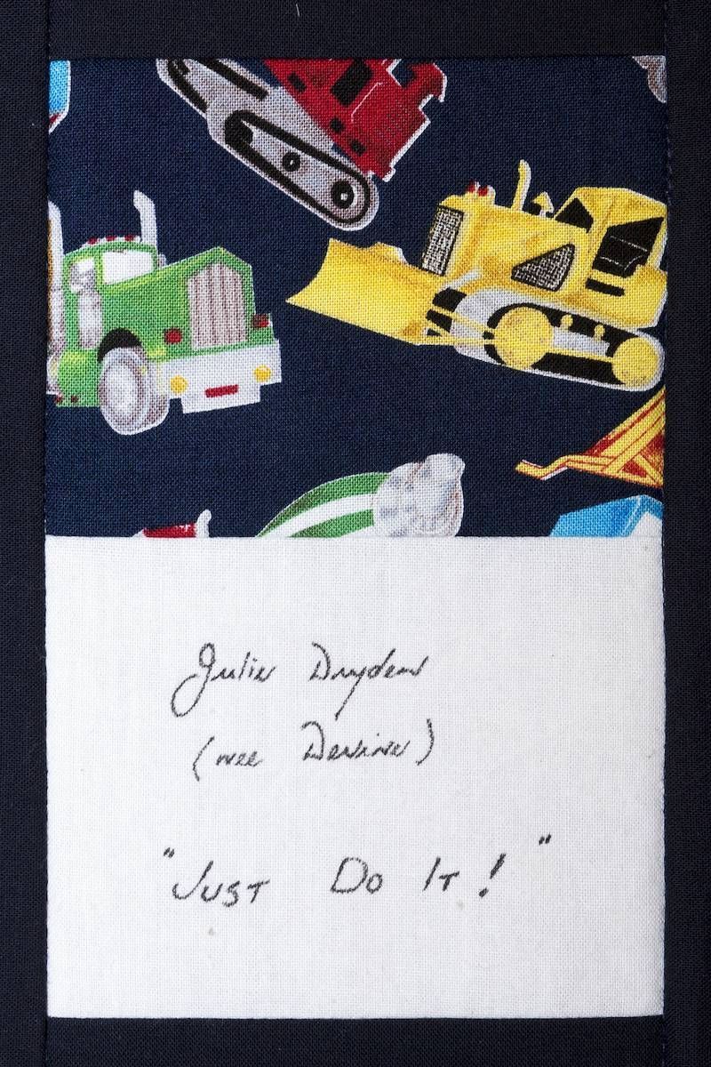 Handwritten note on white paper over colorful toy construction trucks on a dark patterned background.