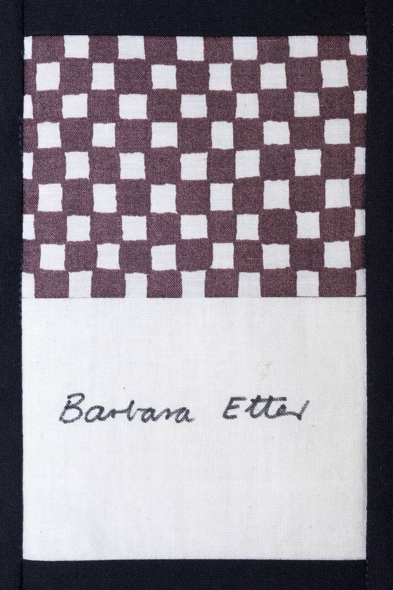 Brown-and-white checkerboard fabric sample with handwritten label near the bottom
