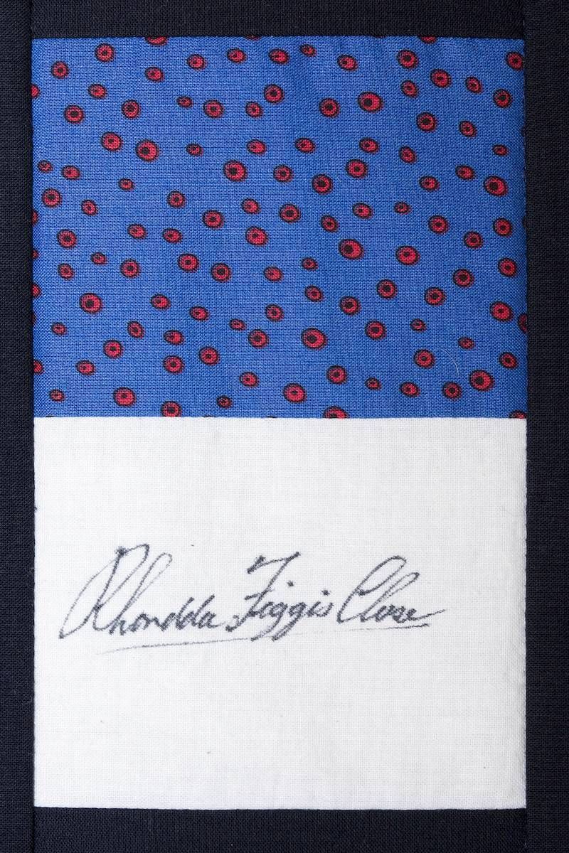 Blue patterned fabric above white paper with a cursive handwritten signature