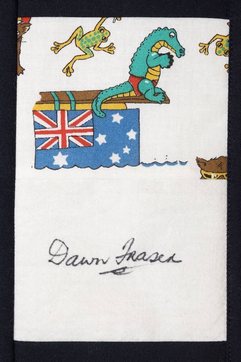 Cross-stitched Australian flag with a green cartoon dragon and handwritten name “Dawn Fraser” below
