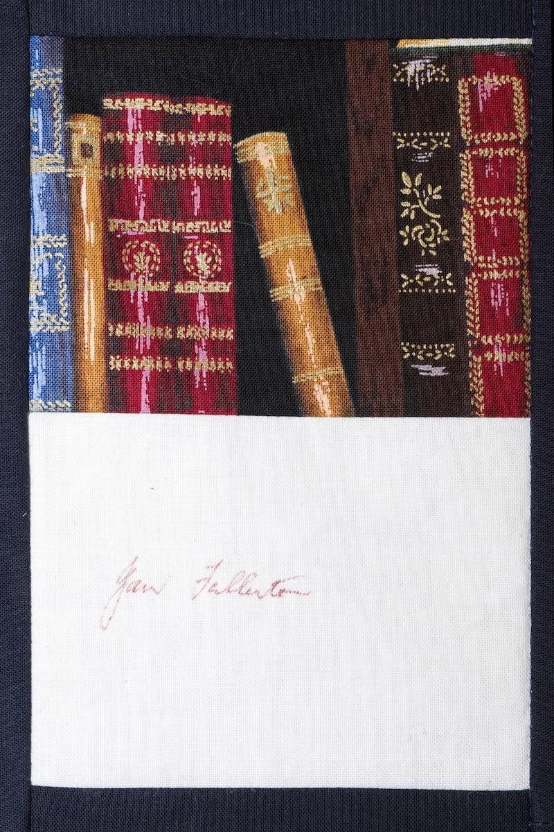 Books on a shelf with a white label across the bottom and faint red writing.
