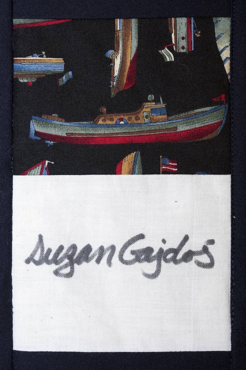 White patch with handwritten cursive text “Suzan Gajdos” on a dark fabric background.