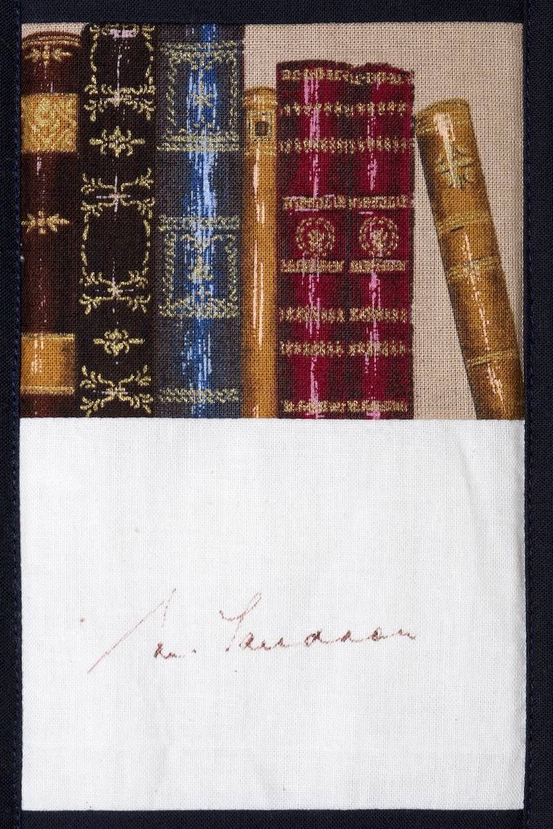 Row of ornate leather-bound books above a blank white card with a faint handwritten signature