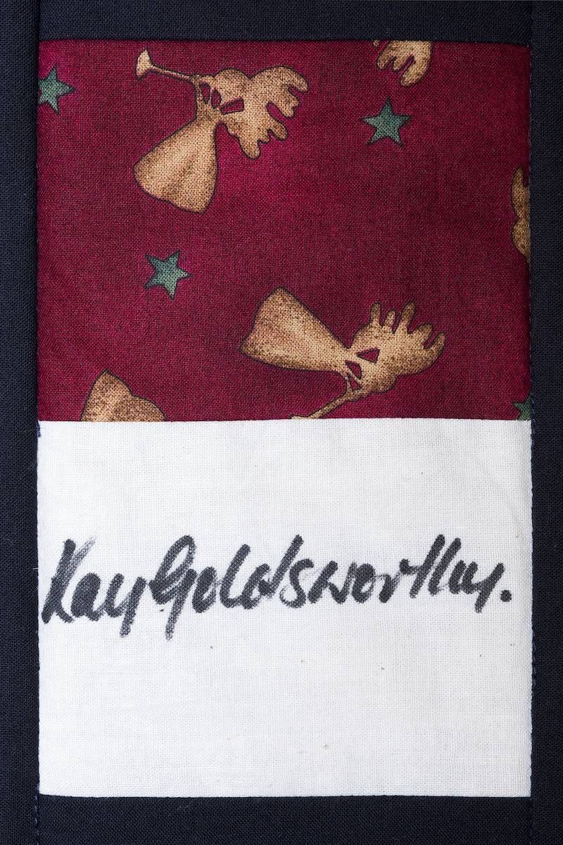 Maroon patterned fabric label with handwritten black text on a white strip