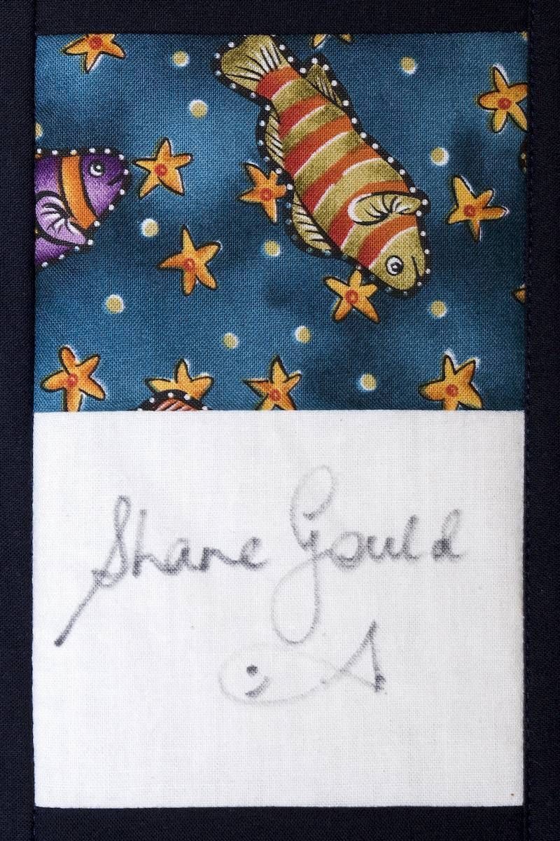 Handwritten note reading “Shine Gold” below a colorful fish and star pattern on blue fabric