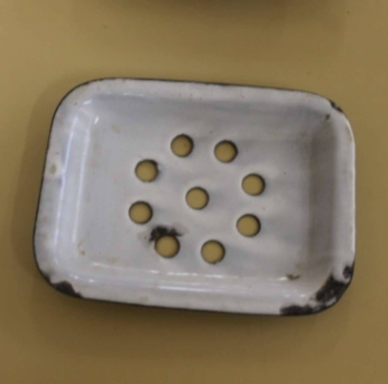 White metal tray with eight small round holes on a beige surface