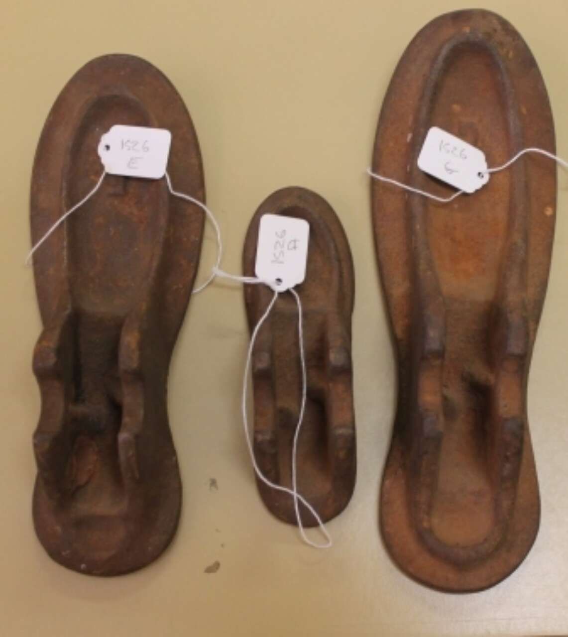Three rusted metal shoe insoles with white tags on a beige background