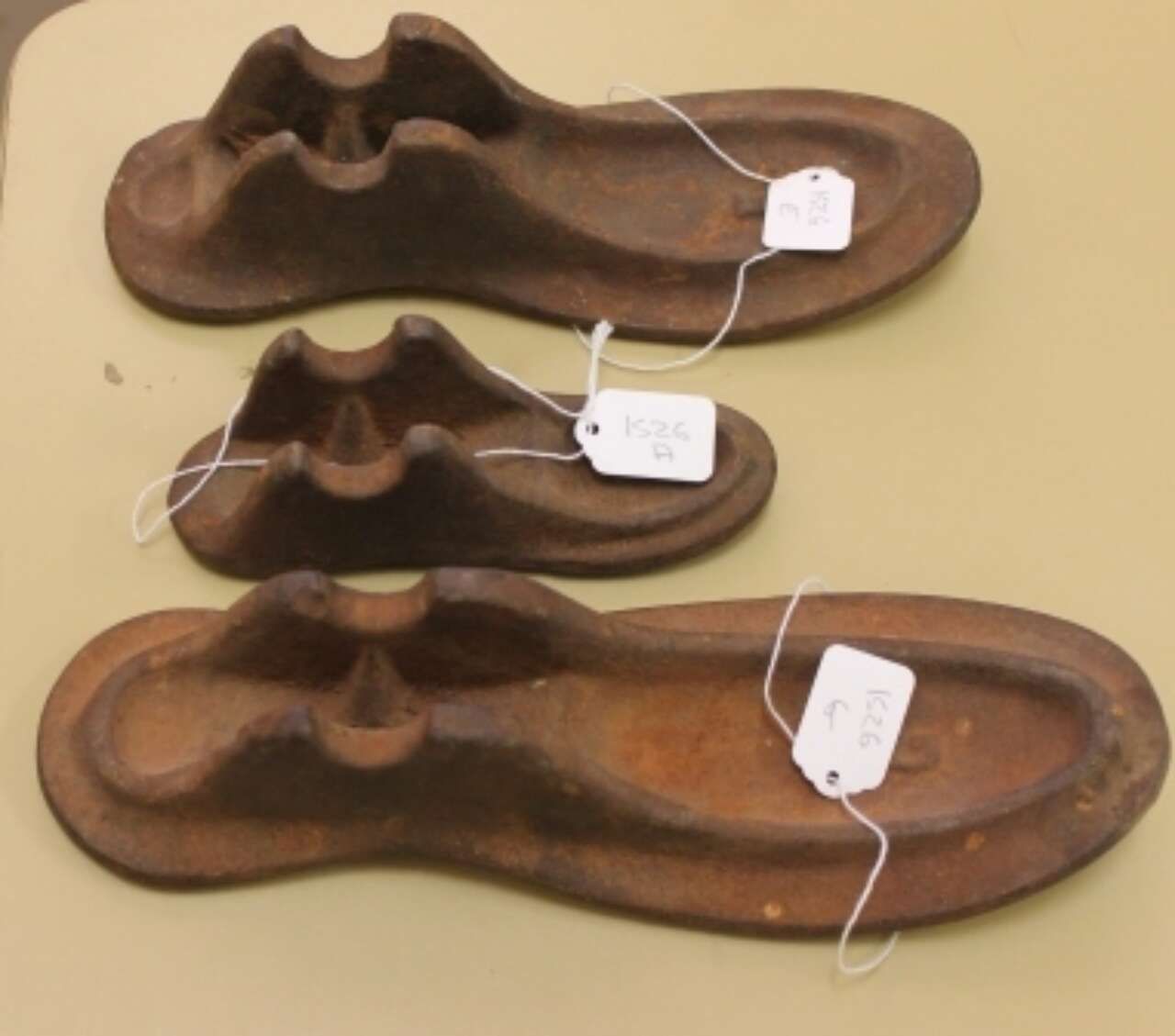 Three brown carved wooden shoe lasts on a beige surface, each with a small white tag attached.