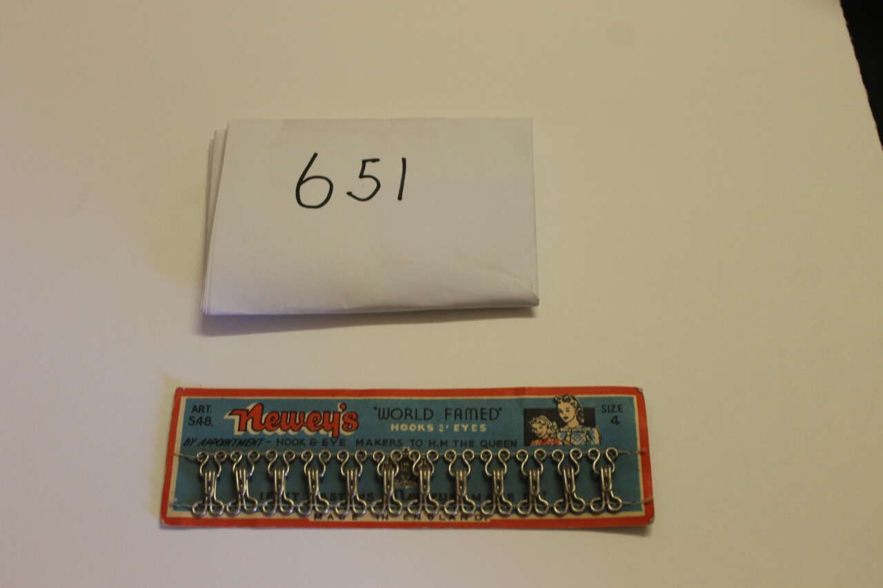 Folded note labeled “651” above a small blue-orange blister pack of miniature figures on a beige surface