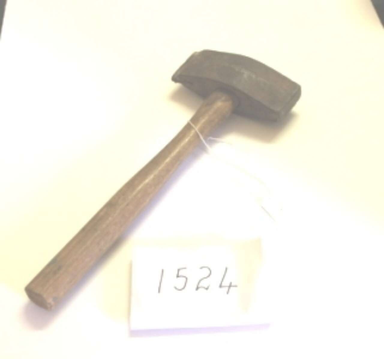 Black hammer with wooden handle lying on a white surface beside a small label reading 1524.