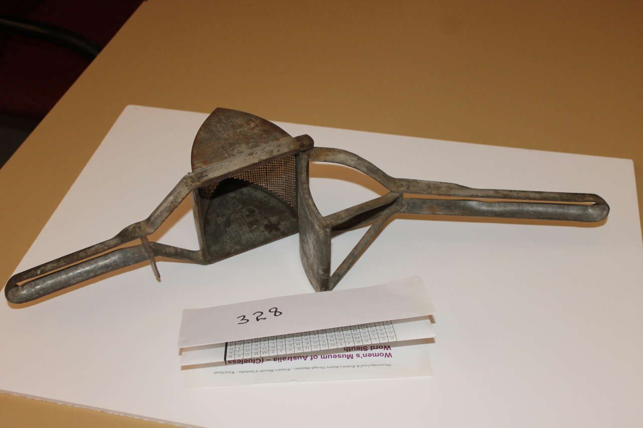 Rusty metal tool with a boxy center and long handles on a table, beside a small label strip