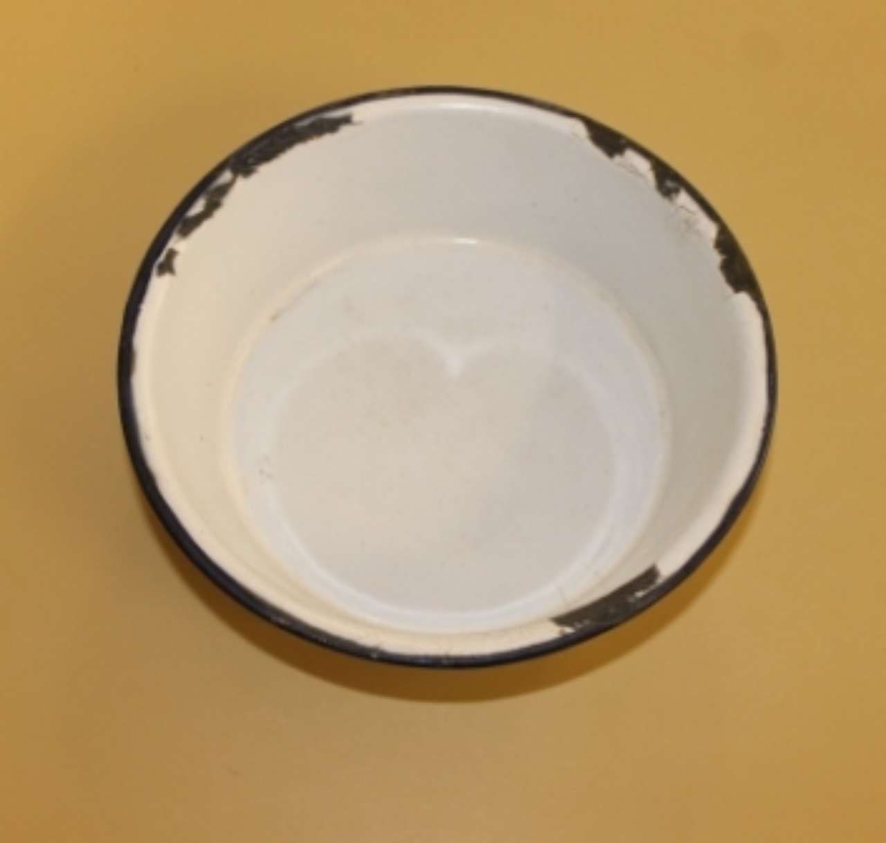 White enamel bowl with black rim on a tan surface