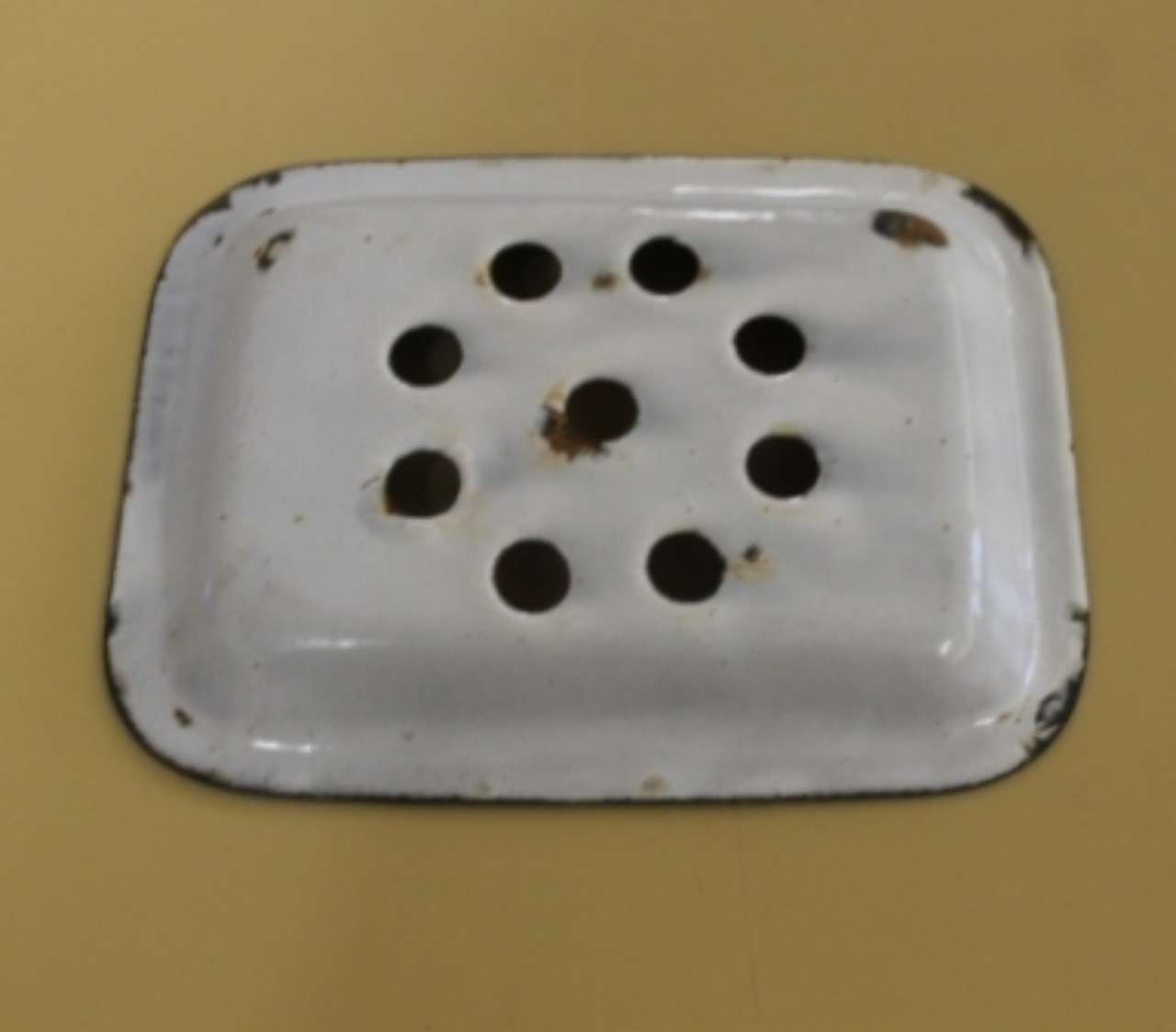 White perforated metal drain cover on a beige surface.