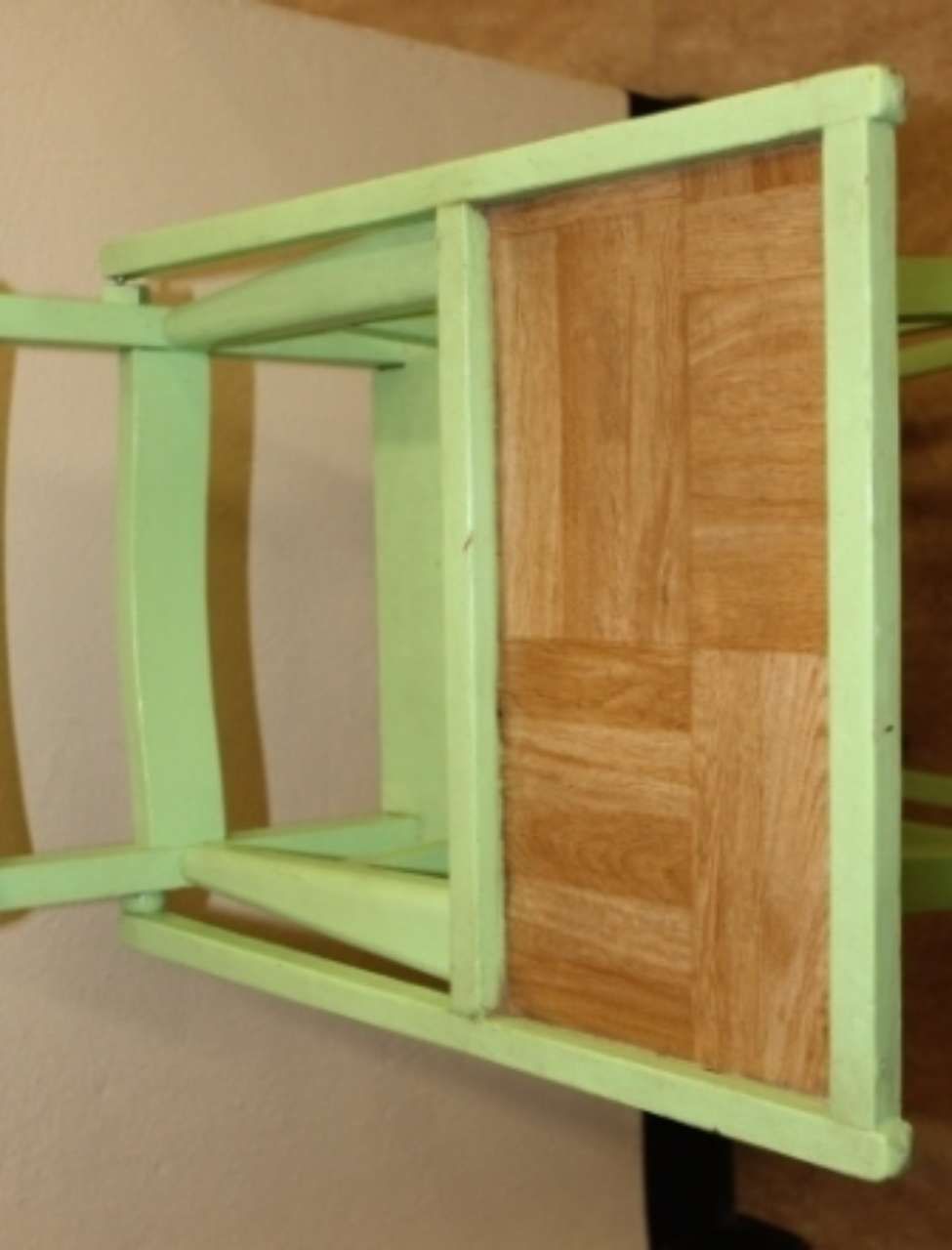 Light green wooden chair with woven seat, viewed sideways against a tan wall