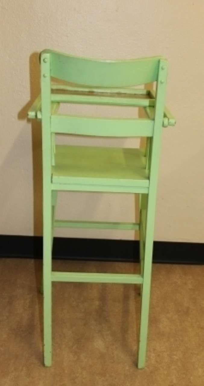 Mint-green wooden high chair against a beige wall on a wooden floor