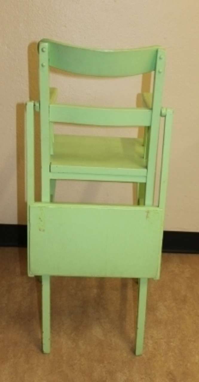 Light green wooden high chair with tray against a beige wall and wood floor