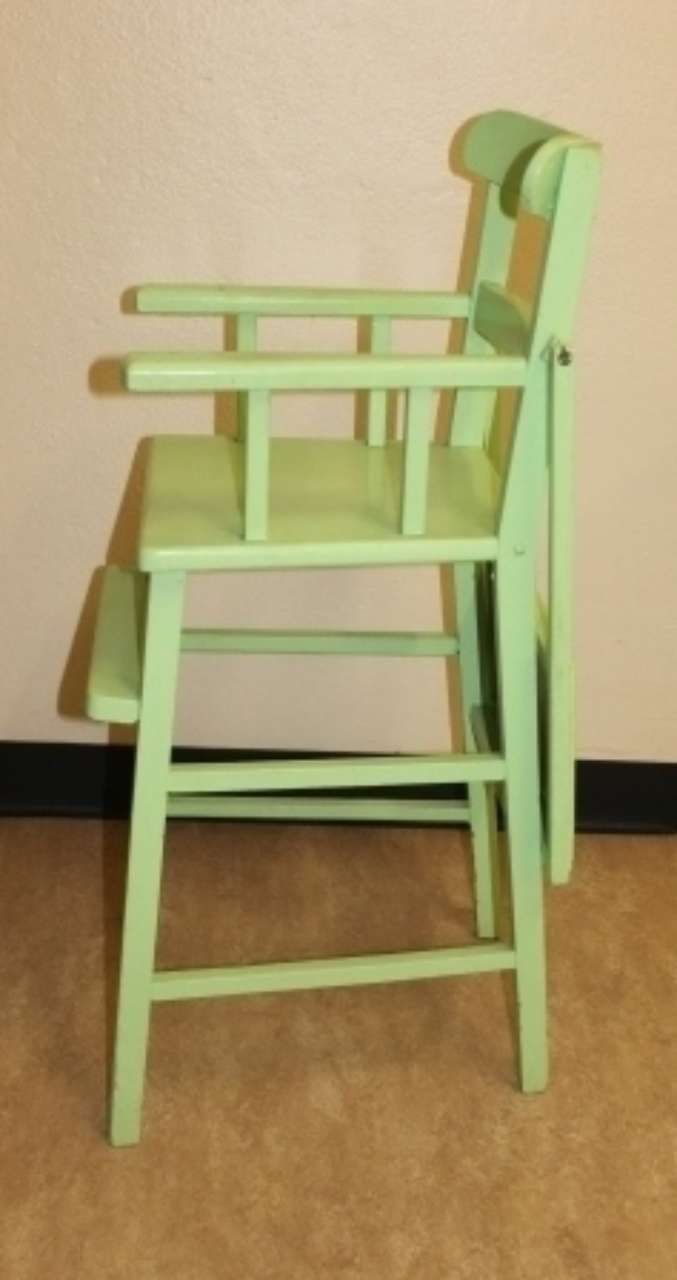 Light green wooden high chair against a beige wall on a brown floor.