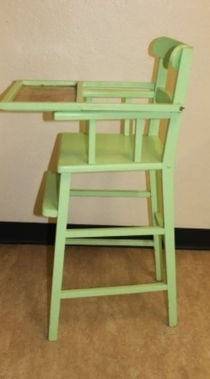 Mint green wooden high chair with tray, side view, standing on a wood floor against a beige wall